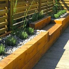 a wooden bench sitting next to a garden filled with flowers and plants in front of a fence