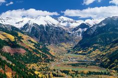 the mountains are covered in snow and green trees with yellow leaves on them, as seen from above