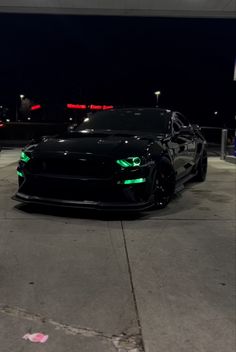 a black sports car parked in a parking lot at night with neon lights on it