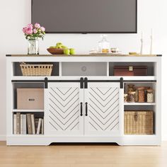 a white entertainment center with sliding doors and baskets on the bottom shelf in front of a flat screen tv