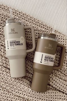 two travel mugs sitting next to each other on a blanket