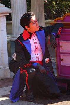 a man dressed in black and red is leaning against a purple chest on the sidewalk