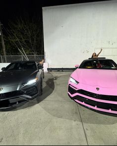 two pink and black sports cars parked next to each other in front of a white building