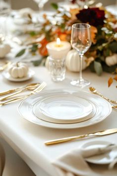 the table is set with white plates and gold cutlery, candles, and flowers