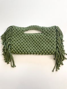 a crocheted green purse with fringes on the bottom and sides, sitting on a white surface