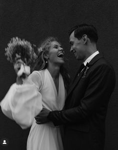 a man standing next to a woman in a white dress and holding a flower bouquet