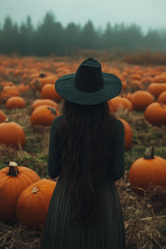 a woman with long hair wearing a black hat standing in a field of pumpkins