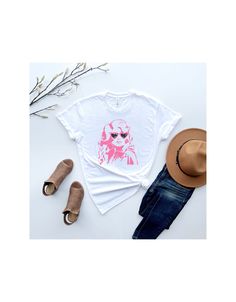 This Dolly Parton tee is a must-have for all you wild-hearted gals out there. Featuring our beloved Queen of Country herself, rockin' a pair of heart-shaped sunnies, this shirt is guaranteed to turn heads and start conversations. Perfect for bachelorette parties or just a night out with your besties, this tee will let everyone know you're here to have a good time and live your best life, Dolly-style. And let's be real, who wouldn't want to channel that level of confidence and badassery? So if yo Unisex Pink T-shirt With Funny Print, Trendy Unisex Pink Top, Trendy Pink Top With Sublimation Print, Unisex Pop Culture T-shirt For Summer, Unisex Pink T-shirt For Spring, Summer Pop Culture T-shirt, Pink T-shirt For Spring, Pink Pop Culture Tops For Spring, Trendy Pink T-shirt With Front Print