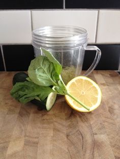 a blender sitting on top of a wooden counter next to a lemon and spinach