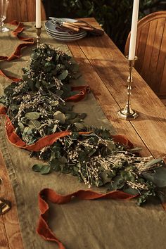 a long table with candles and greenery on it, along with other place settings