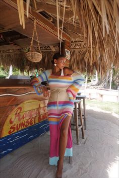 a woman in a colorful dress standing under a straw hut