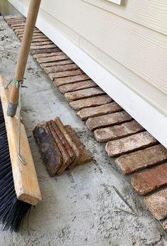 a broom is laying on the ground next to some bricks and a brick walkway that has been laid in front of a house