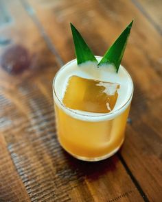 a drink with a green leaf sticking out of it's top sitting on a wooden table