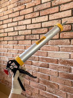 a person holding a large metal object in front of a brick wall with scissors attached to it