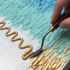 someone is painting the letters on a canvas with gold and blue paint while using a brush