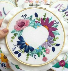 someone is holding up a heart shaped embroidery kit in front of some other embroidered items