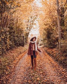 a woman walking down a leaf covered road