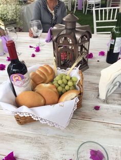 a basket filled with bread and grapes on top of a table next to a bottle of wine