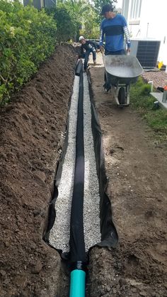 two men are working in the garden with hoses attached to drainage pipes that have been dug into the ground