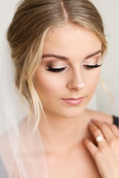 a woman wearing a veil and makeup looks down at her wedding ring on her finger