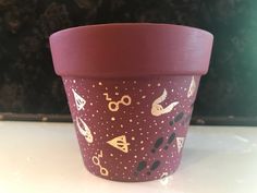 a purple cup with gold designs on it sitting on a white counter top next to a black wall