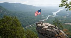 an american flag is on top of a rock overlooking a valley and river in the distance