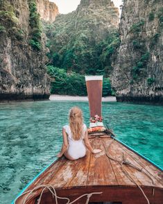 a woman sitting on top of a boat in the middle of blue water with cliffs behind her