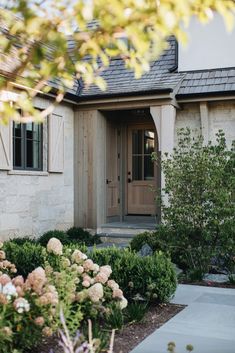 the front door of a house with flowers and shrubs around it, along with an entry way