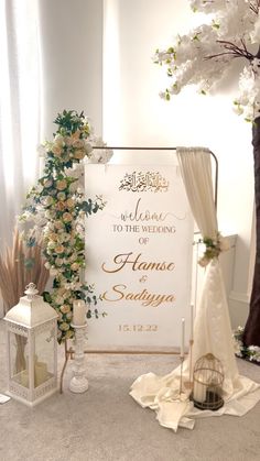 a welcome sign with flowers on it next to a wedding arch and lantern lanterns in the background