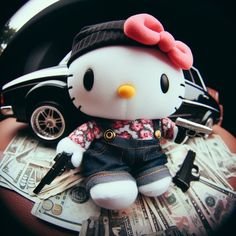 a hello kitty doll sitting on top of money with a car in the back ground