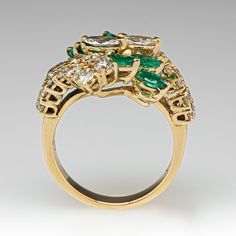 This pretty ring is centered with a cluster of two (2), prong set, marquise brilliant cut diamonds and six (6), prong set, marquise mixed cut natural emeralds. The top face of the by-pass style shank is accented with twenty-six (26), prong set, round brilliant cut diamonds. The ring measures 18.0mm at the top, rises 8.0mm above the finger, tapering to 2.9mm wide and 1.1mm thick at the base of the shank. This ring is currently a size 7. Marquise Multi-stone Diamond Ring, Luxury Multi-stone Marquise Cut Diamond Ring, Luxury Marquise Cut Multi-stone Diamond Ring, Luxury Marquise Emerald Ring For Wedding, Luxury Marquise Emerald Wedding Ring, Marquise Brilliant Cut Emerald Ring, Marquise Emerald Ring With Brilliant Cut, Fine Jewelry Marquise Cut Emerald Ring With Diamond Accents, Elegant Marquise Cut Multi-stone Cluster Ring