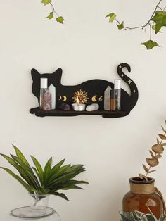 a black cat shelf with candles and bottles on it next to a potted plant