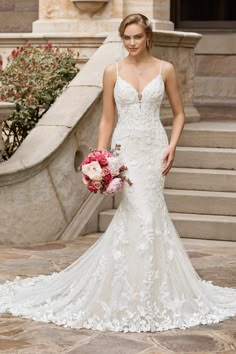 a woman in a wedding dress standing on steps holding a bouquet and looking at the camera