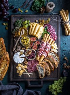 an assortment of cheeses and meats on a cutting board with breadsticks