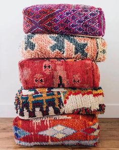 a stack of colorful rugs sitting on top of a wooden floor next to a wall