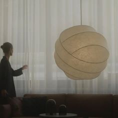 a woman standing in front of a couch next to a lamp hanging from the ceiling