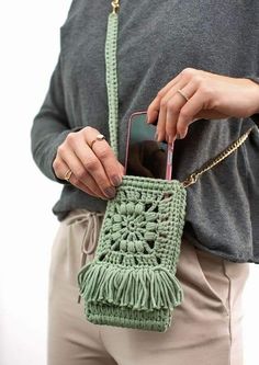 a woman holding a green crochet purse with a cell phone in her hand