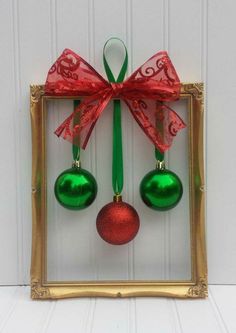 two christmas ornaments hanging from a gold frame with a red bow and green ornament