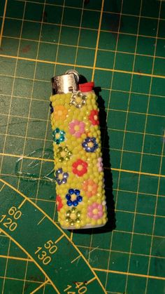 a lighter is covered in beads on a green mat with a ruler next to it