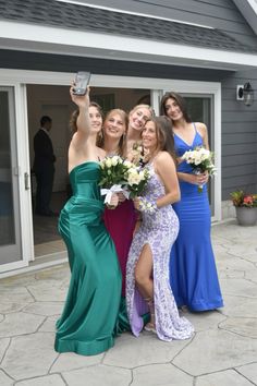 four women pose for a photo in front of a house wearing dresses and holding bouquets