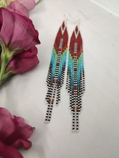 two pairs of beaded earrings sitting next to pink flowers