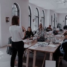 a group of people sitting around a wooden table in a room with arched windows on the walls