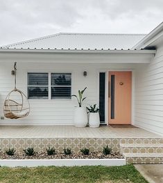 a white house with two planters and a hanging chair on the front door porch