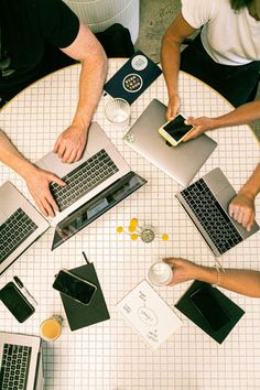 four people sitting at a table with laptops