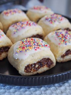 several pastries with white frosting and sprinkles on a black plate