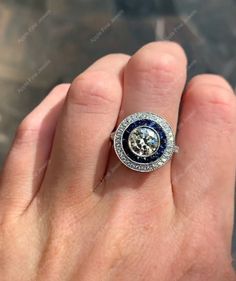 a person's hand is holding a ring with a blue and white diamond center