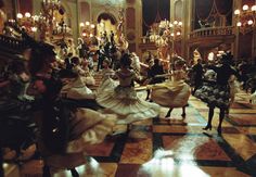 a group of people dressed in costume dancing on a dance floor with chandeliers hanging from the ceiling