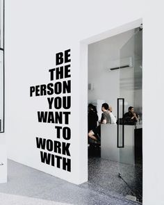 a man sitting at a desk in front of a wall with the words be the person you want to work with