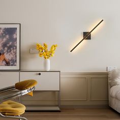 a room with a couch, chair and pictures on the wall above it that has yellow flowers in a vase