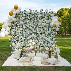 a white and gold wedding arch with balloons, flowers and pillows on the ground in front of it